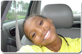 A young girl smiles while sitting in the passenger seat of her car.